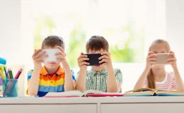 Trójka dzieci przy stole wpatrzonych w w swoje smartfony